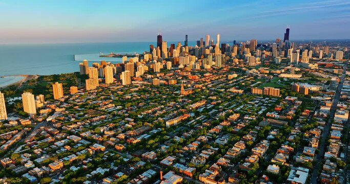 Green uptown and high-rise downtown of Chicago, Illinois in the rays of setting sun. Amazing blue waterscape of Lake Michigan at backdrop.