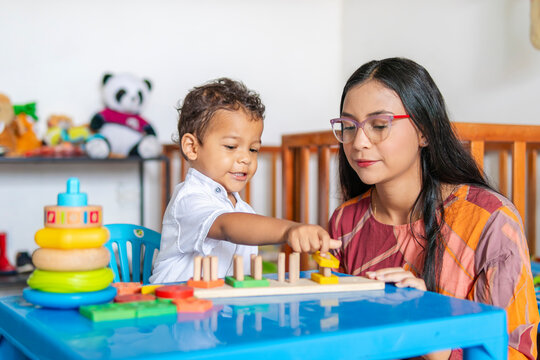 Young Latina mother in her 20s, single, playing with her 2-year-old son in the nursery, where the crib and various toys are visible in the background