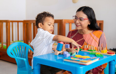 Single Latina mother watches her child interact and play with wooden blocks of different colors...