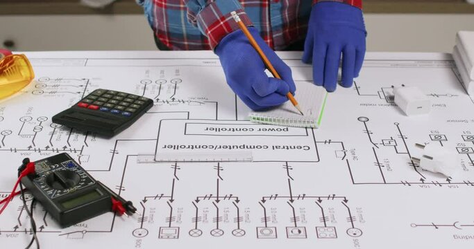 Technician checks circuit network drawing and marks notes at table closeup. Electrician plans installation with on schematic diagram blueprint