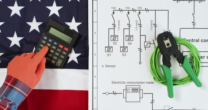 Engineer counts on calculator near schematic diagram put on American flag upper view. Contractor checks electrical plan of circuit network