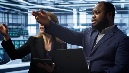 Teamworking colleagues in server farm using laptop to patch network issues affecting transfer rates. Coworkers in data center doing brainstorming, fixing errors affecting supercomputers, camera A