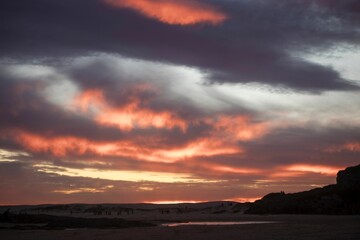 Obraz premium Stunning sunset over a sandy beach with people silhouetted against the colorful sky.