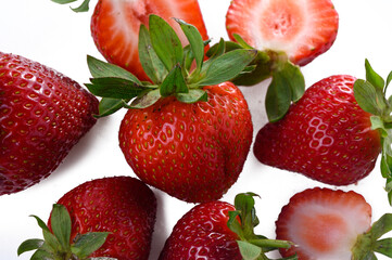 Fresh ripe strawberries and green leaves falling on white background