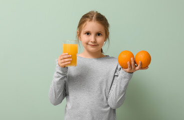 Cute little girl with glass of juice and oranges on green background