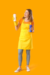 Young woman with bottles of detergent on orange background