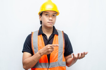 asian man consrtruction worker wearing yellow safety helmet and orange vest smiling and pointing finger to copy space with happy and surprised expression.