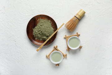 Composition with cups of fresh matcha tea, powder and accessories on light background