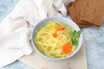 Bowl of tasty chicken soup and bread on blue background