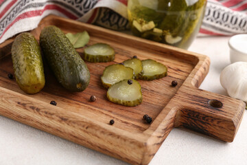 Wooden board with tasty canned cucumbers on white background
