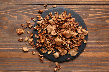 Black board with tasty dried mushrooms on wooden background