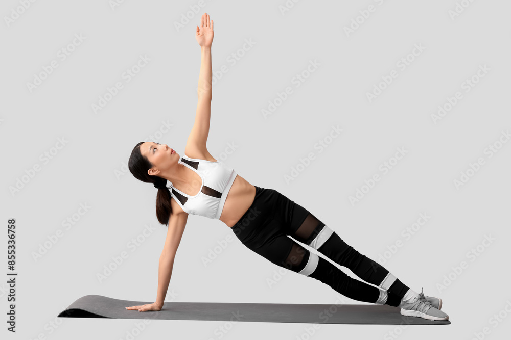 Canvas Prints Sporty young Asian woman training on mat against light background