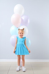 Cute little girl with beautiful balloons near grey wall