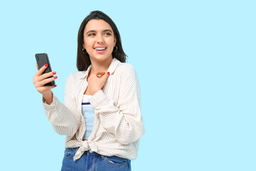 Young woman with mobile phone on blue background. Online dating concept