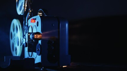 A vintage movie projector in operation. Blue light illuminates the film reels, creating a cinematic atmosphere. The background is dark, highlighting the projector - Powered by Adobe