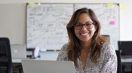 Smiling professional woman working on a laptop, whiteboard in background, office environment