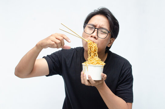 young Asian man enjoys his noodles with deep pleasure using chopstick and paper bowl. man in black tshirt eats noodles with great enthusiasm.