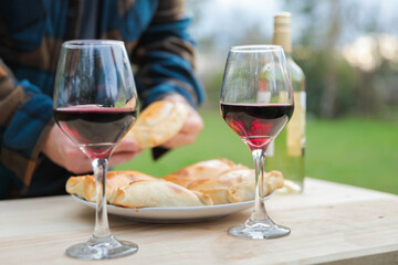 Unrecognizable man picking typical chilean oven empanada beside wineglass and bottle of red wine. Fiestas patrias