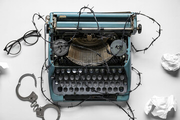 Vintage typewriter with barbed wire, handcuffs and crumpled paper on white background. Printing ban...