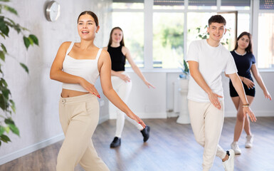 Obraz premium Female teen performs choreographic exercises and teaches energetic mobile social dance vogue together with friends. Young girls and guy repeat movements, train in spacious studio