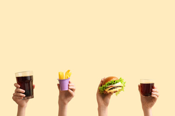Female hands with tasty burger, french fries and glasses of cola on light yellow background