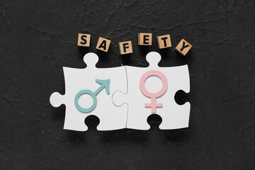 Puzzle pieces with female, male symbols and cubes with word SAFETY on dark grunge background. Sex...