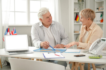 Obraz premium Mature couple with world map planning their trip at table in travel agency