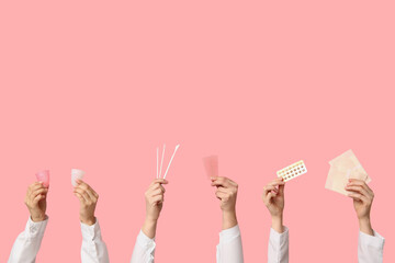 Doctor's hands with menstrual cups, pads, pills and pap test tools on pink background