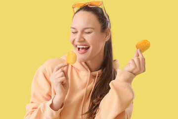 Young woman eating potato chips on yellow background, closeup