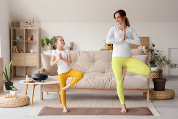 Young woman with her little daughter doing yoga on mat at home