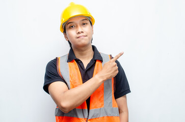 asian man consrtruction worker wearing yellow safety helmet and orange vest smiling and pointing finger to copy space with happy and surprised expression.