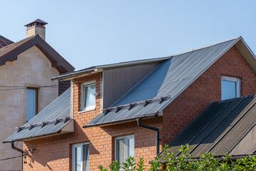 Close-up view of a brick house with a metal roof. The house has a dormer window and a chimney. The...