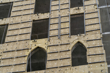 Close-up of building under construction with insulated beige panels on exterior walls. Two arched windows, metal strips, and white dots visible