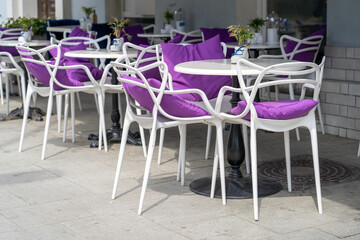 White chairs with purple cushions are arranged around tables on a patio