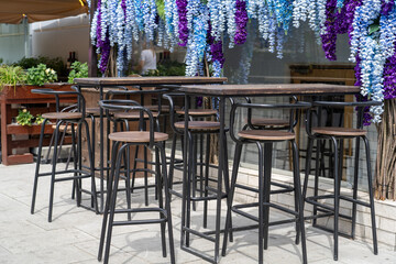 A view of a small outdoor bar with black metal stools and tables decorated with purple and blue flowers