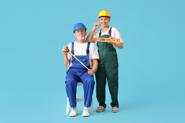 Mature couple of decorators with tape measure and level on blue background