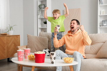 Young father and little son with soccer ball watching football at home