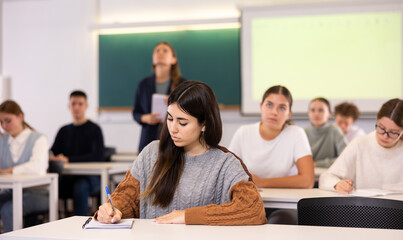 Obraz premium A young female student is carefully recording a lecture by a school teacher