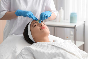 Beautician removing woman's hair on face with wax strip in salon, closeup