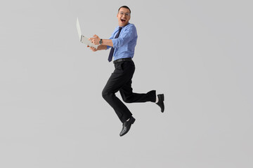 Handsome businessman with laptop jumping on light background