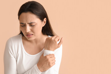 Young woman suffering from pain in wrist on beige background, closeup