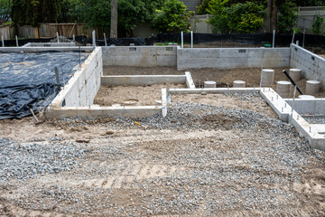 New home foundation construction in progress, cement retaining walls in place, cement poured and curing in round pylon support forms, residential building site
