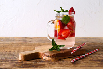 Mason jar of fresh infused water with strawberries, lemon and mint on  wooden table