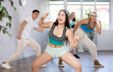 Fototapeta premium Group of young women and young guy perform hip hop dance moves in dance hall