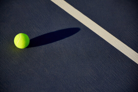 A tennis ball on tennis court with court lines and shadows