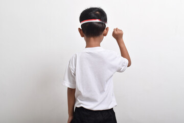 Back view of cute little Asian boy with happy success attitude wearing flag headband isolated on white background. Indonesia's independence day concept.