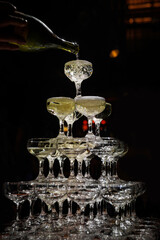 Waiter pouring champagne on a pyramid tower on a dark background.