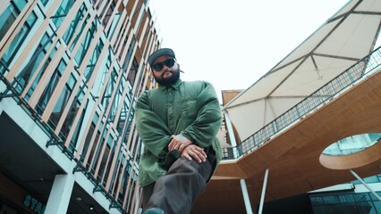 Low angle view of hipster pose in hip hop style surrounded by mall view. Portrait of sporty asian hip hop choreographer dancing break dance while looking at camera. Outdoor sport 2024. Endeavor.