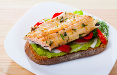 Tasty piece of bread with fried trout fillet, onion, pepper and guacamole