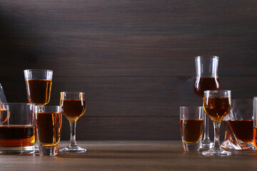 Different delicious liqueurs in glasses on wooden table, space for text